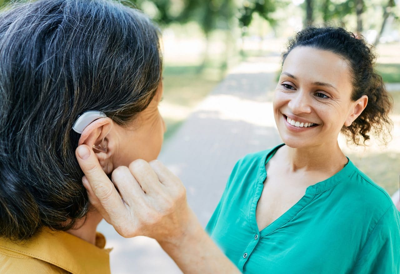 Woman with hearing aid chatting with her friend outdoors.