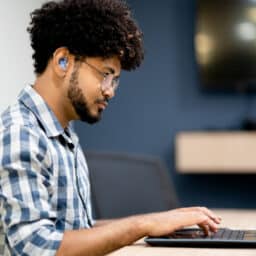 Side view of man with hearing aids working on laptop at office