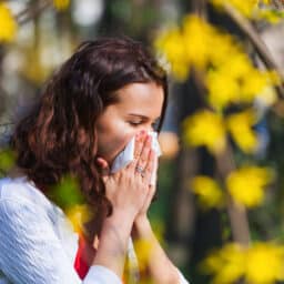 Woman blows nose near trees