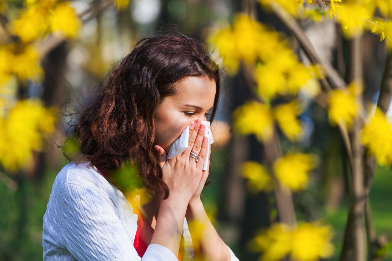 Woman blows nose near trees