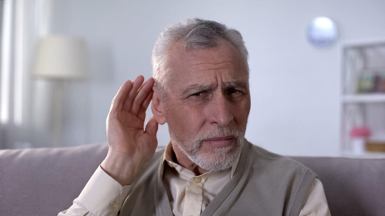 Senior man looking confused with a hand up to his ear.