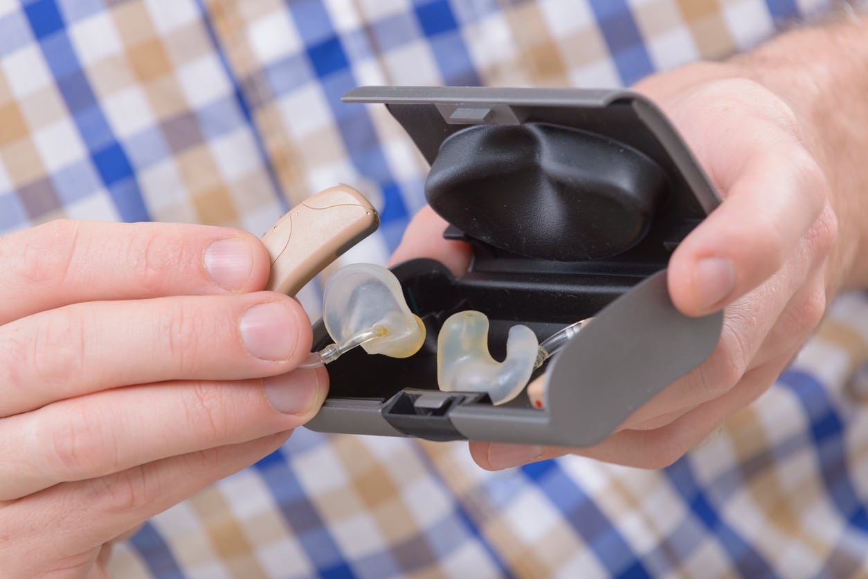 Close-up of a man holding hearing aids in their case.