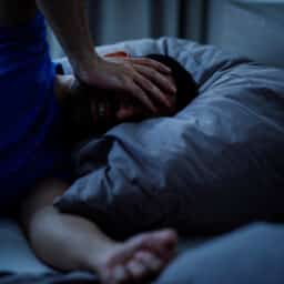 Man touching his head with insomnia and headache symptom while lying in bed in modern indoor bedroom