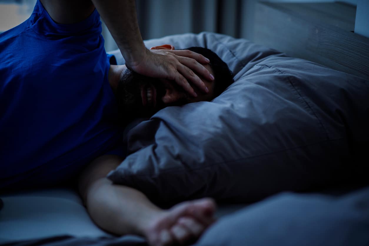 Man touching his head with insomnia and headache symptom while lying in bed in modern indoor bedroom