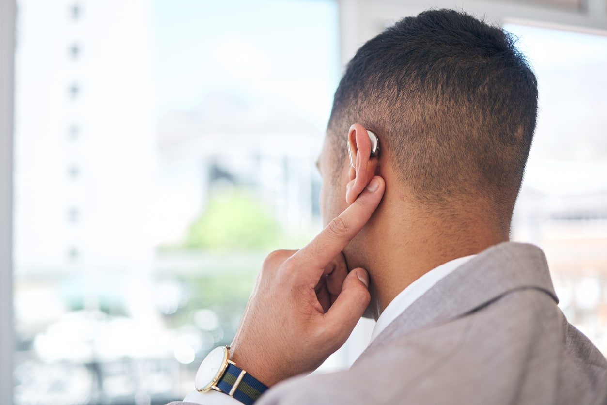 Rear view of a man pointing to his hearing aid.