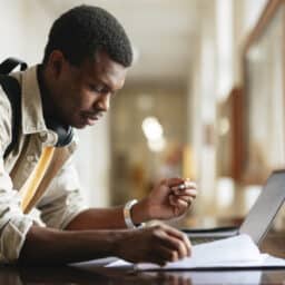 Focused university student engaging in study using a laptop in a bright hallway.