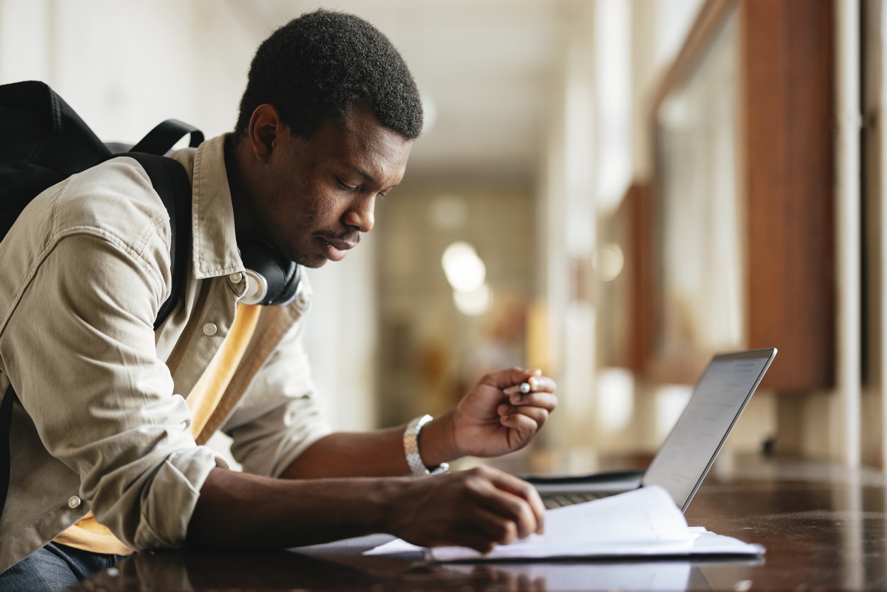 Focused university student engaging in study using a laptop in a bright hallway.